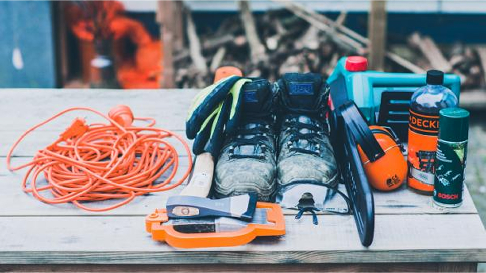 A collection of outdoor/work tools and equipment arranged on a wooden surface